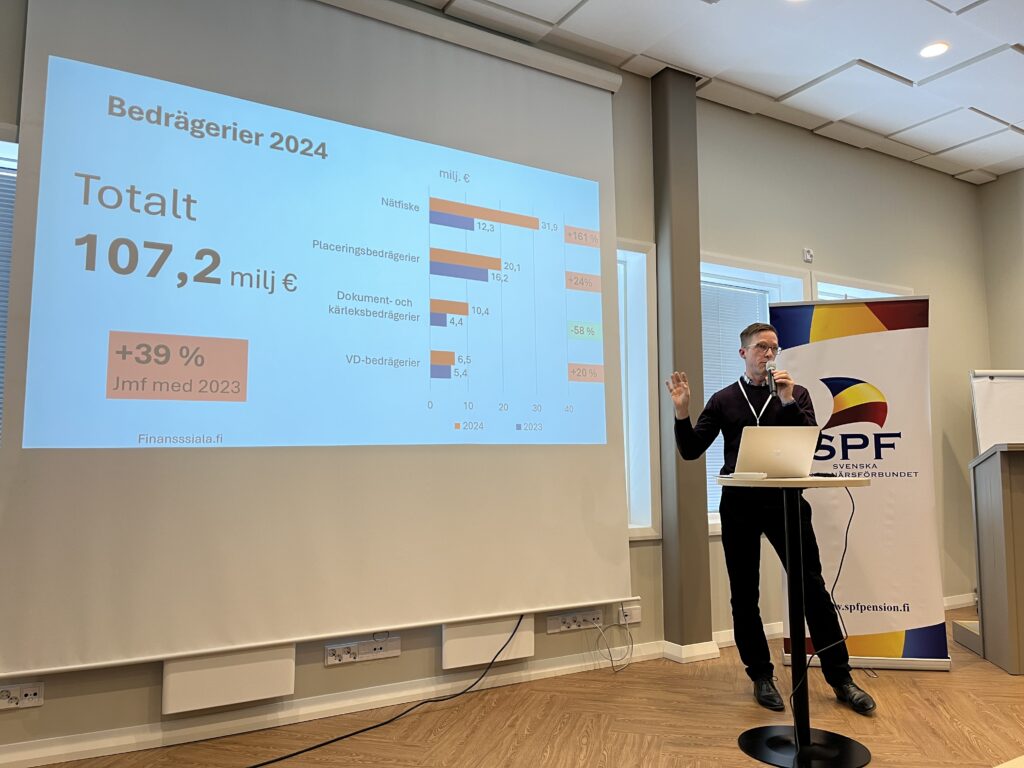 En man står vid ett talarstativ och håller ett föredrag. På en stor projicerad bild visas finansiella uppgifter för 2024, bland annat siffran 107,2 milj € och ett stapeldiagram. Till höger om föredragshållaren syns en 5PF-banner.