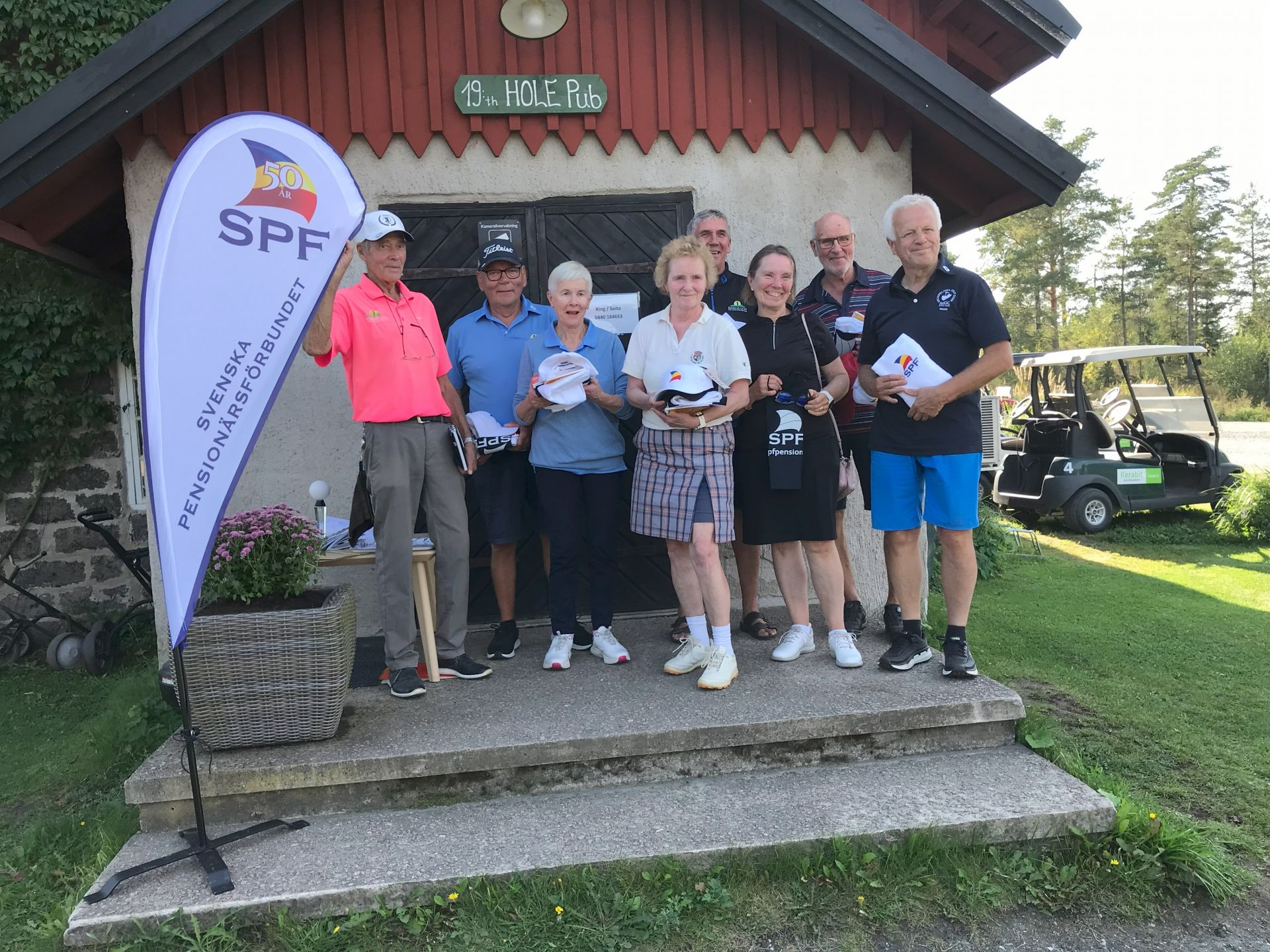 En grupp på åtta äldre personer står på en veranda med priser i händerna och ler. Till vänster syns en banderoll för Svenska Pensionärsförbundet. I bakgrunden syns en golfbil och gräs.