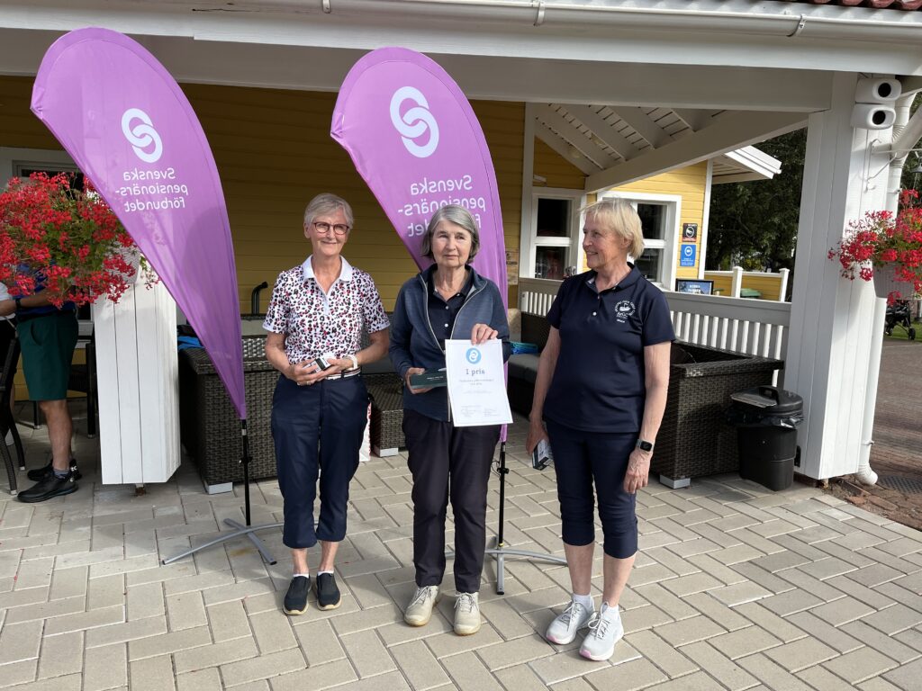 Tre kvinnor står utomhus på en uteplats framför en gul byggnad. Två av dem håller i glastroféer och en håller i ett diplom. I bakgrunden syns två rosa flaggor med vita logotyper.